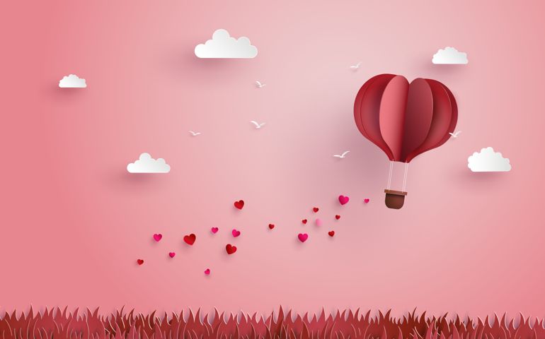 Origami made hot air balloon flying over grass with heart float on the sky
