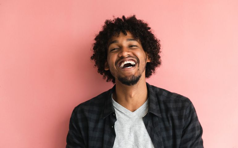 Casually dressed African-American guy posing in front of pink background.