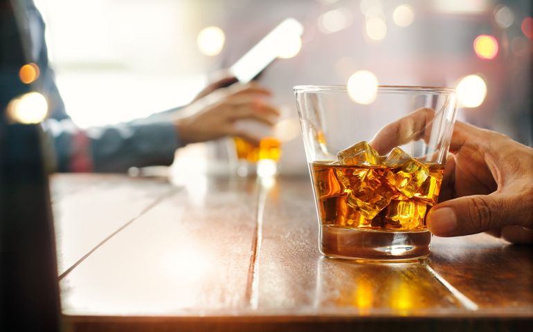 Close-up of two men clinking whiskey drink alcoholic beverage at bar counter in the pub background.