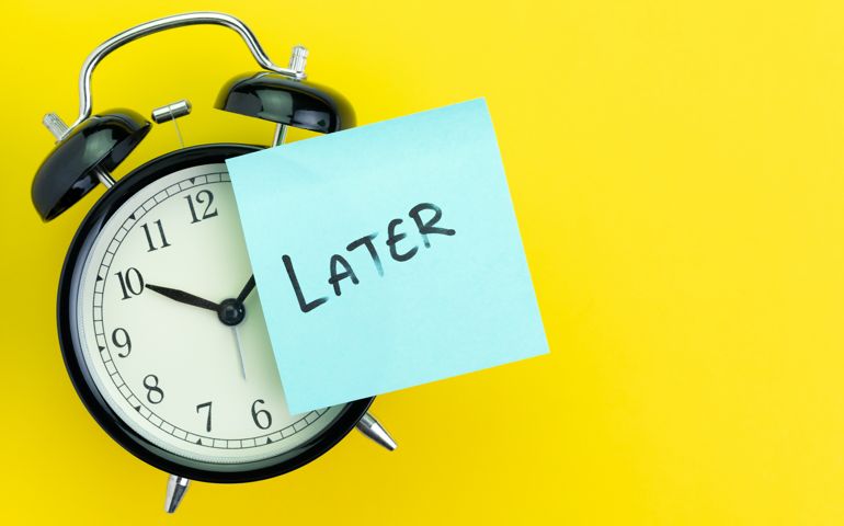 Sticky post with handwriting the word Later stick on alarm clock on solid yellow background with copy space using as procrastination, self discipline or laziness concept.