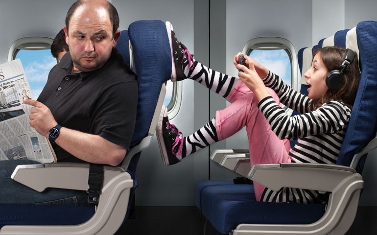 A carefree young girl annoying the passenger in front by pushing his seat.