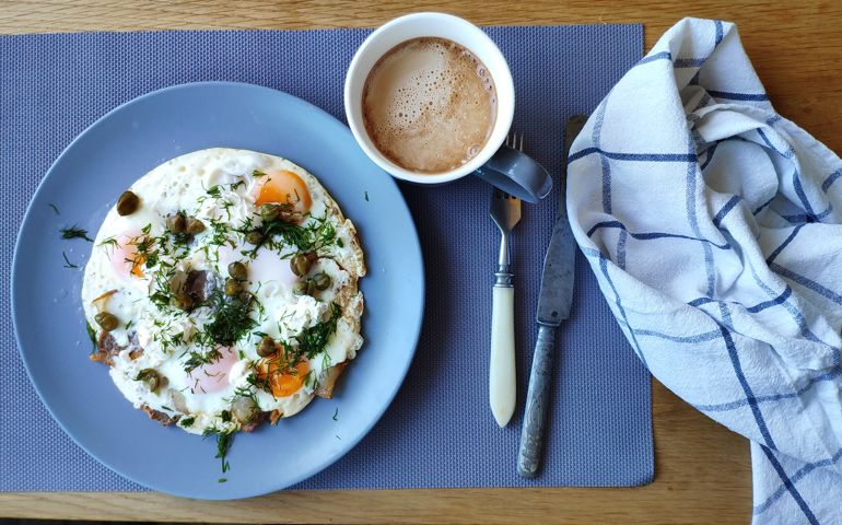 Fried eggs with capers and herbs and coffee with cream, ketogenic breakfast concept, selective focus