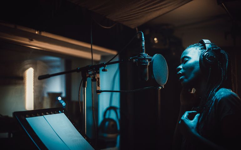 One woman, beautiful black female vocalist wearing headphones and singing into microphone in recording studio.