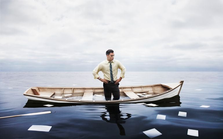 A 32 year old Caucasian man dressed in business attire (minus coat) standing in a sinking boat with oars and papers floating away into a glassy overcast sea. He is a businessman trying to solve his business's problems either financial or organizational.