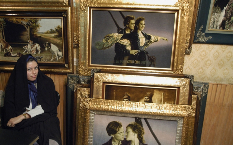 Tabriz, Iran: A woman in black chador sits next to paintings depicting Leonardo DiCaprio and Kate Winslet from the movie 'Titanic'.