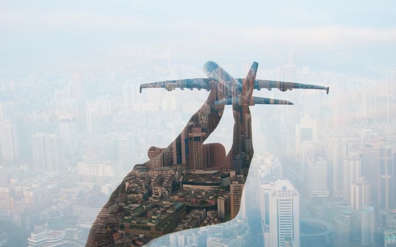 double exposure of mans hand holding a toy plane and cityscape in the background