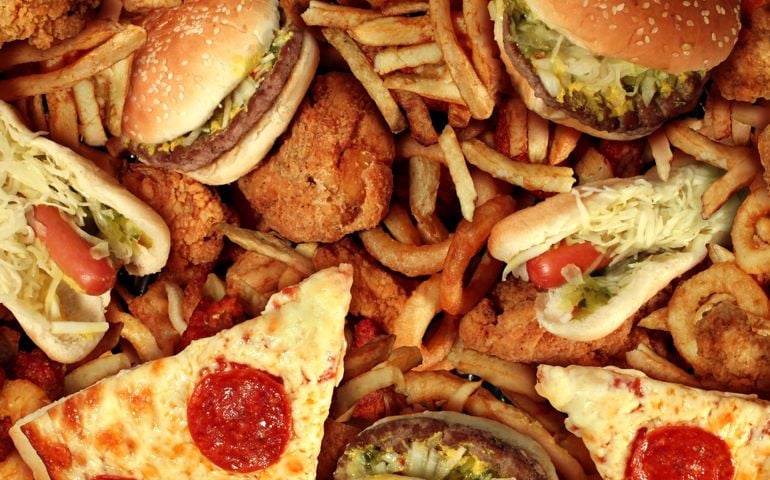Fast food concept with greasy fried restaurant take out as onion rings burger and hot dogs with fried chicken french fries and pizza as a symbol of diet temptation resulting in unhealthy nutrition.