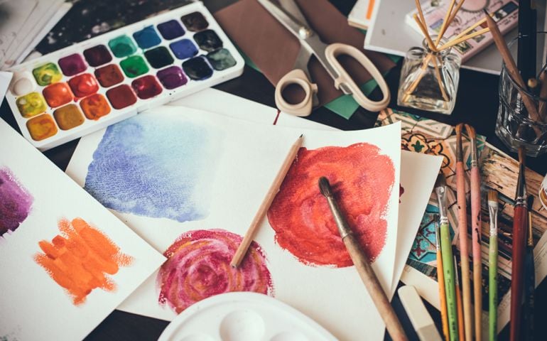 Mess in the the artist's studio, watercolor paints, brushes and sketches, palette and painting tools. Designer's working place, hipster style.