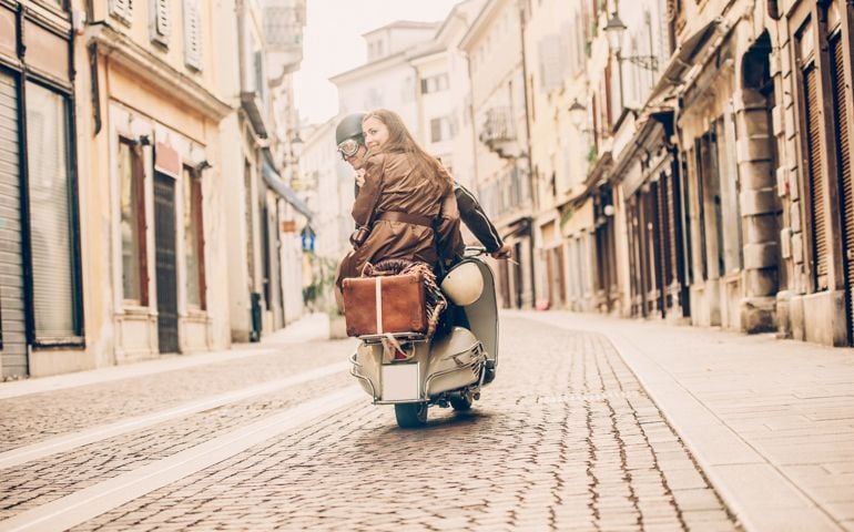 Vintage couple riding scooter in Italy, rear view