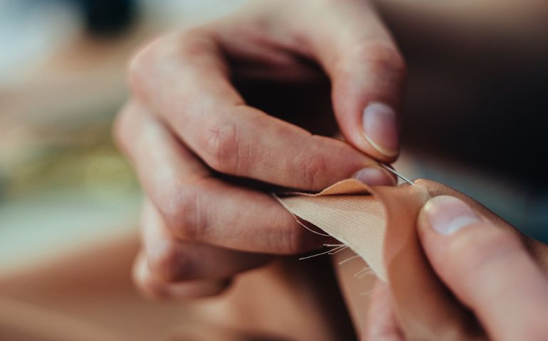 Dress maker working while sewing stitch by-stitch, close-up.