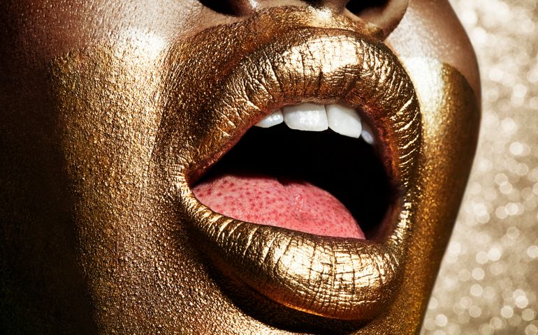Womens mouth and face painted in gold. Open mouth showing tech and tongue