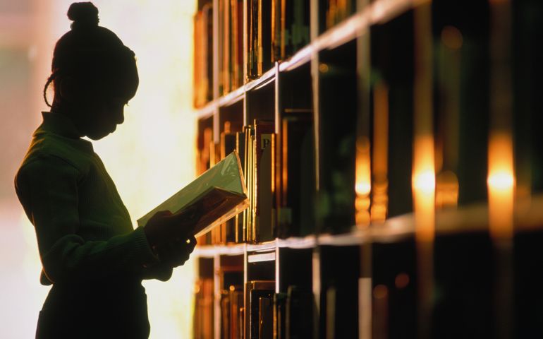 Girl (6-8) looking at book in library, silhouette