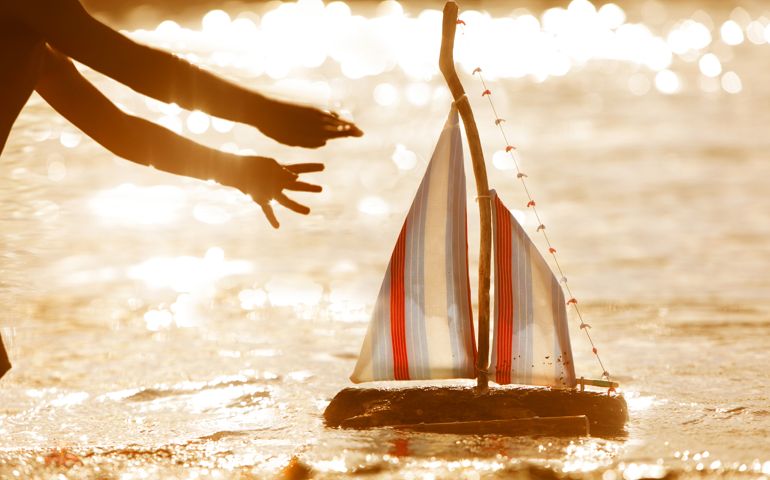 Reaching for toy boat on the water at sunset