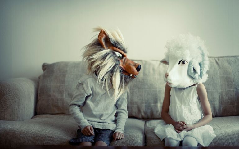 Boy in wolf mask, girl in sheep sitting on sofa.