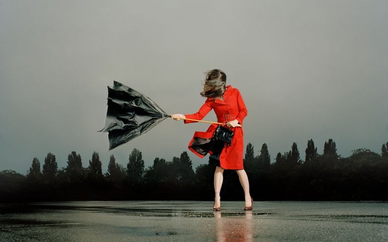 Woman struggling with broken umbrella in rain