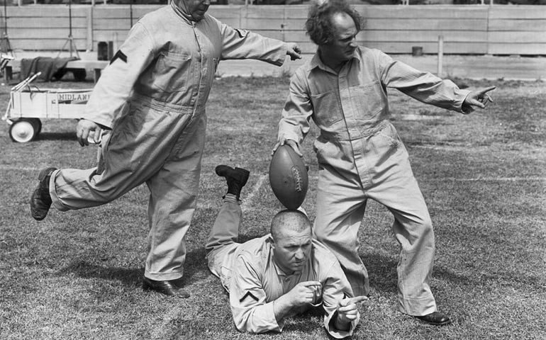 1938: The Three Stooges clowning with a football on a football field, in a still from director Albert Rogell's film 'Start Cheering'. L-R: Moe Howard, his brother Curly Howard and Larry Fine.