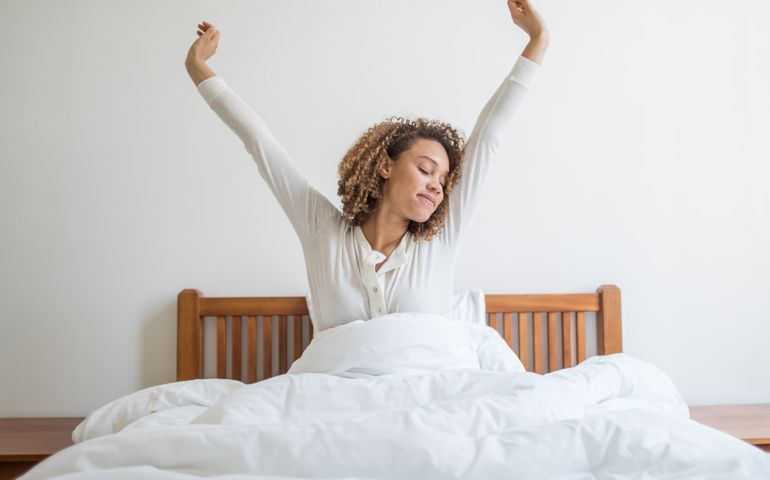 Happy woman yawning in bed waking up in the morning