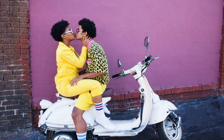 A young couple wearing yellow outfits sitting on a scooter kissing