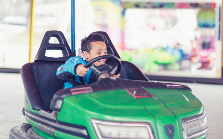 Mixed race boy driving bumper cars in amusement park
