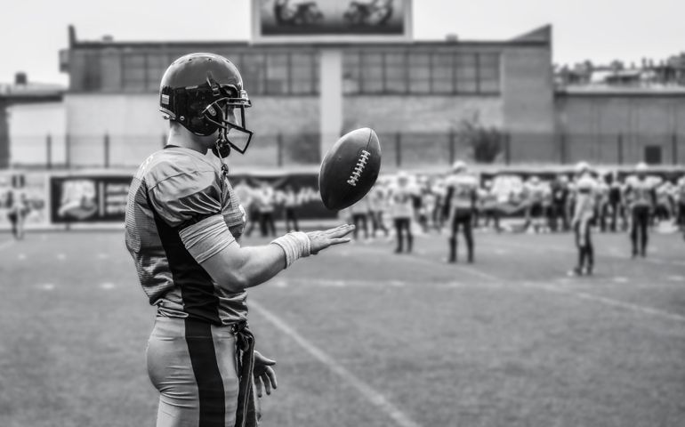 The player of the American football team is throwing the ball with his hand.