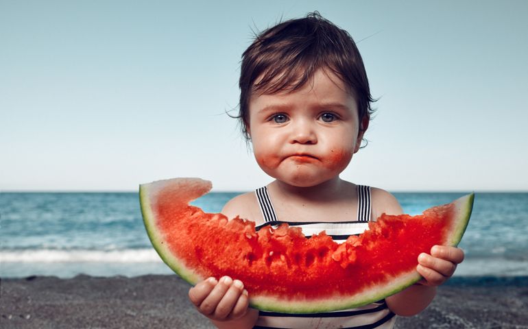 little girl on the beach eating watermelon and making funny face
