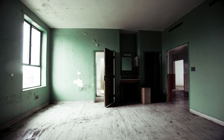 Empty room in an abandoned hospital. Doors open and leading to another creepy room.