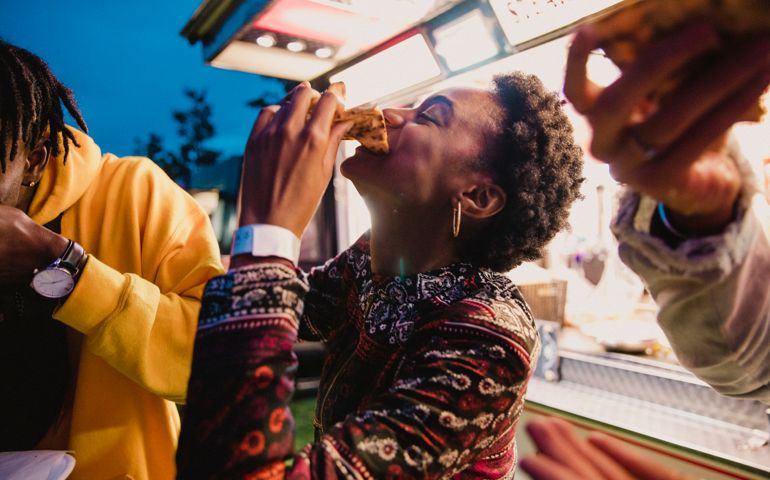 A young women enjoying pizza with friends at a music festival.
