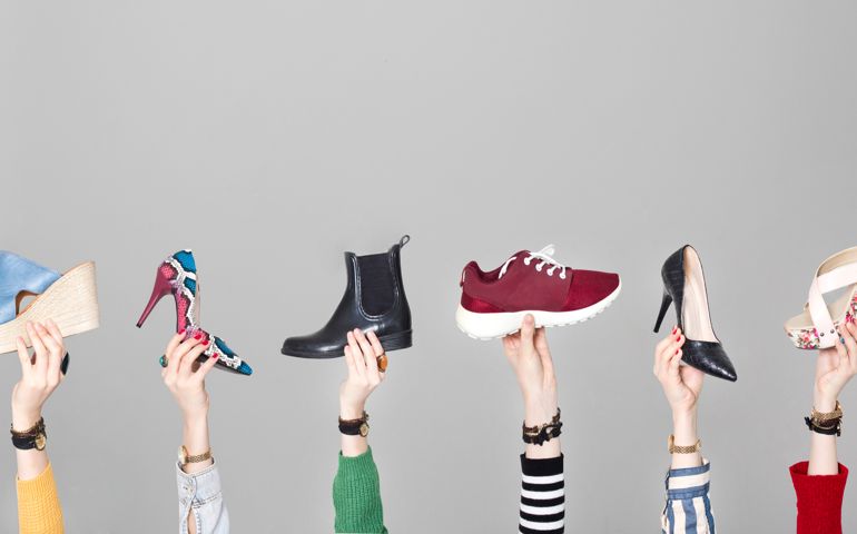 Hands holding different shoes on gray background