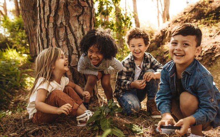 Group of cute kids sitting together in forest and looking at camera. Cute children playing in woods.