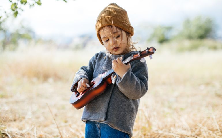Adorable boy with guitar, standing on the grass. Toddler girl playing guitar at sunny countryside home garden