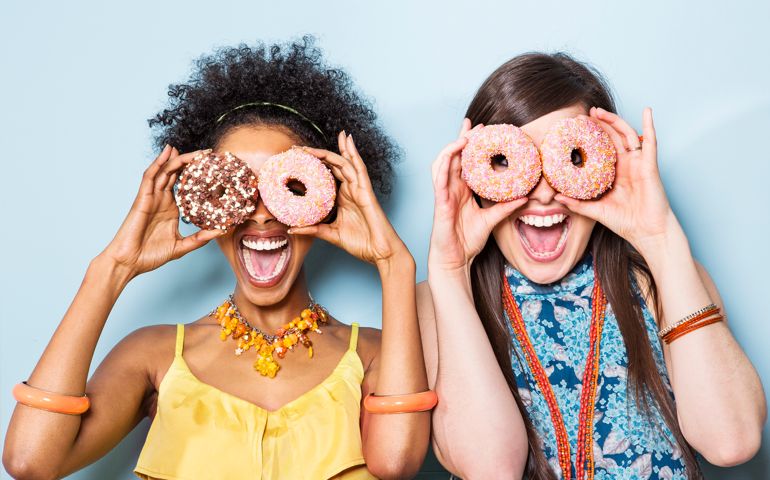 women holding doughnuts in front of eyes.