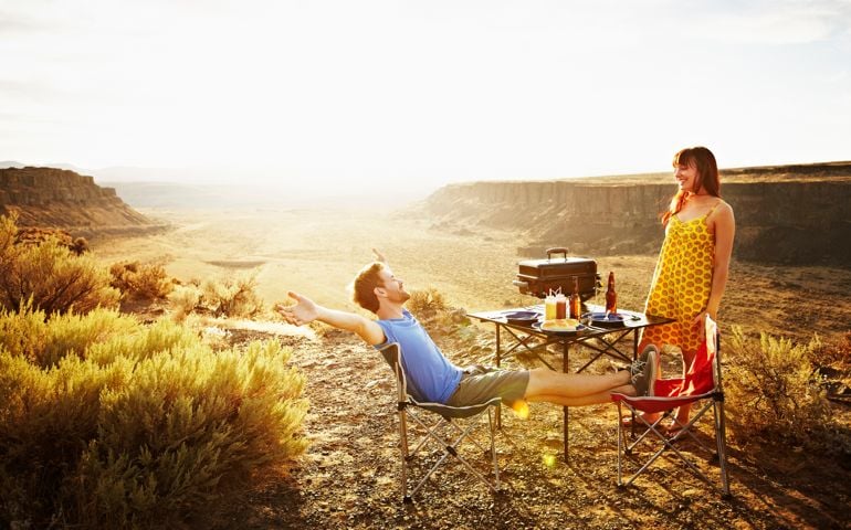 Laughing couple barbecuing at desert valley overlook at sunset