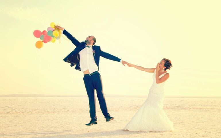 bride and groom wedding photos, groom is flying with balloons and the bride is trying to keep him.