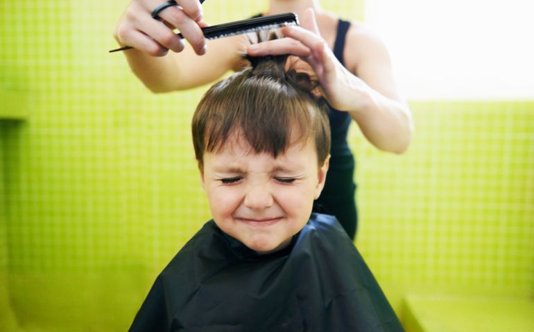 A young boy looking upset as he gets his hair cut in a salon