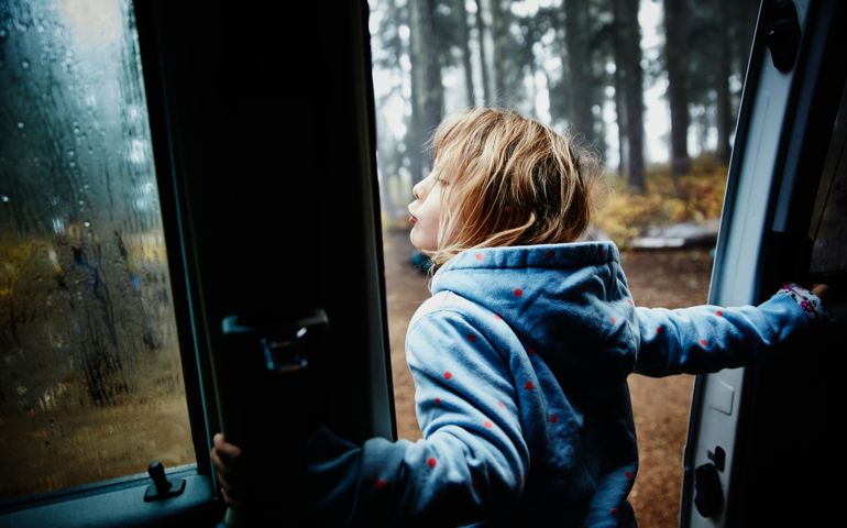 Young girl leaning out door of camper van in the morning while camping with family