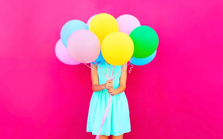 Woman is hides her head an air colorful balloons having fun over pink background