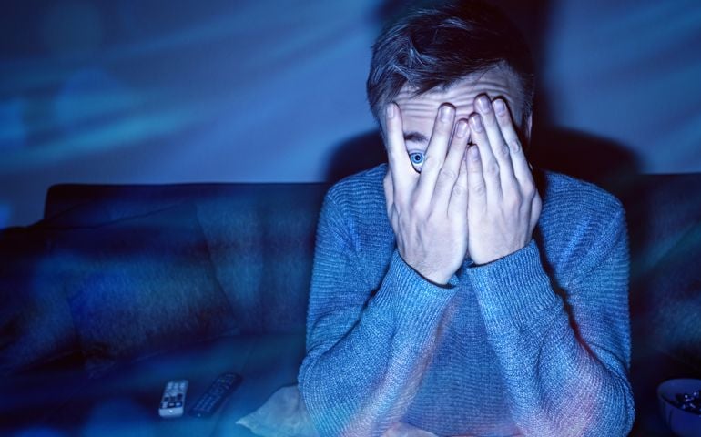 Man covering his eyes while watching TV.