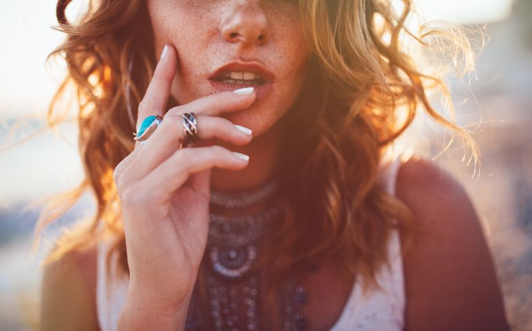 Close-up of bohemian woman with freckles wearing boho style silver turquoise rings and necklaces