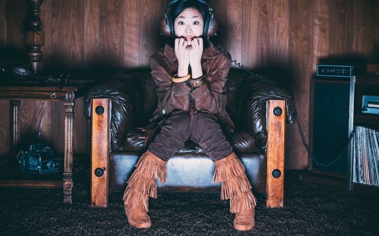 A young Asian woman wearing retro-styled 1970's clothing. Both the model and set are styled to portray a teenager/young adult from 1976 with period correct clothing, furniture, and props.