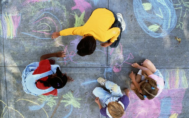 Four children (7-10) drawing with chalk on pavement, overhead view
