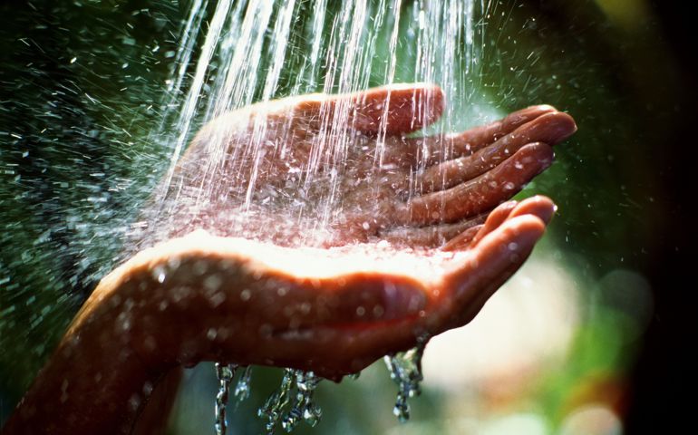 Woman's hands beneath shower of water, outdoors, close-up