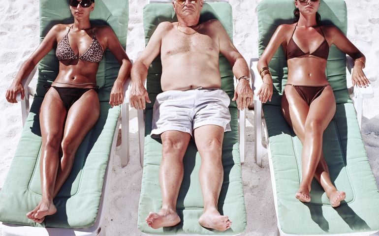 Mature man and two young women on sun loungers on beach