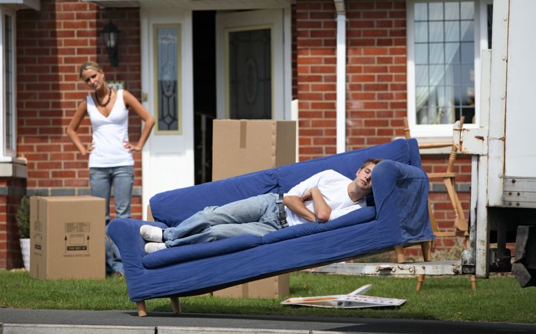 Young man lying down on sofa leaning on truck platform, woman standing in background