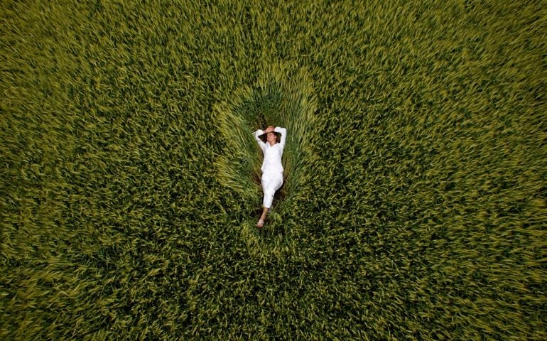 A young woman lies back and relaxes in a field of wheat.