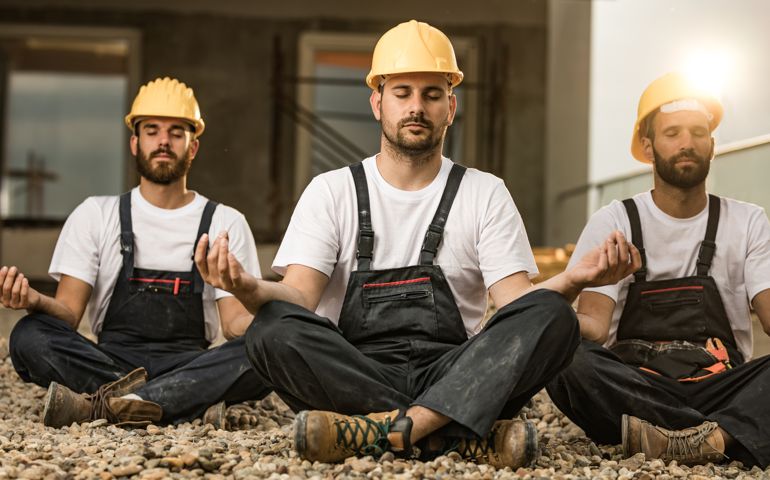 Group of construction workers exercising Yoga in Lotus position during a break at balcony.