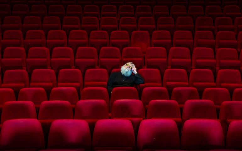 One man with white beard sits in Empty cinema or theatre with comfortable red seats, a sleep
