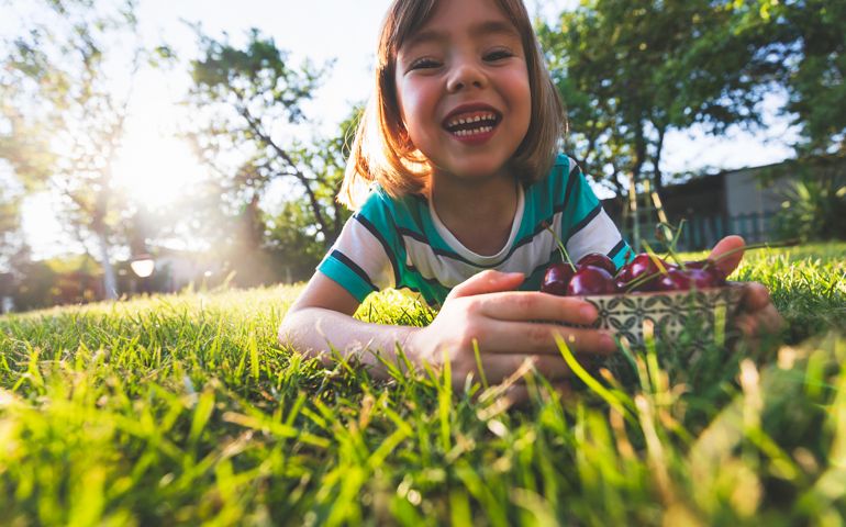 Cute little child holding bowl of cherries.