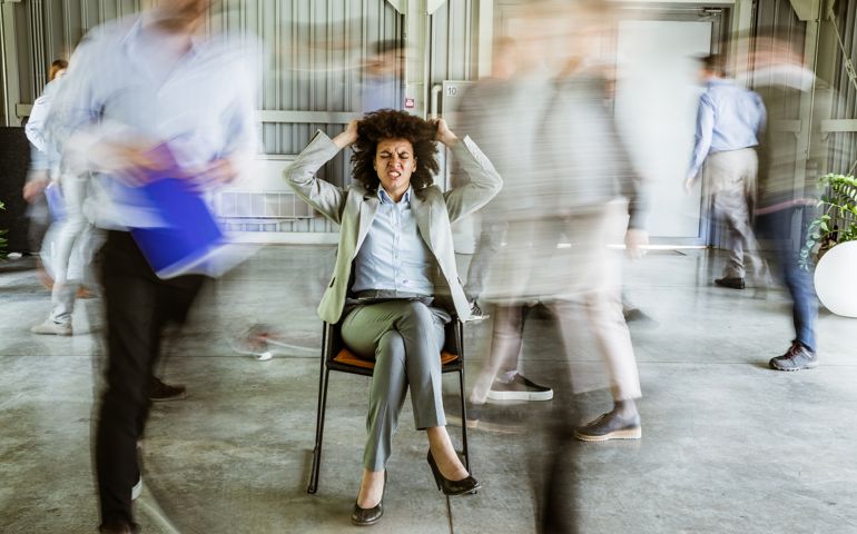 Angry black businesswoman pulling her hair while being surrounded by her colleagues who are walking in blurred motion.