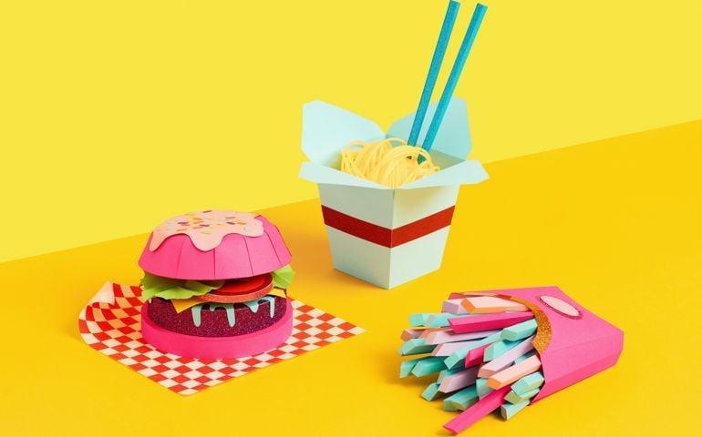 Studio still life image of a paper crafted burger, fries and noodles shot on yellow background.