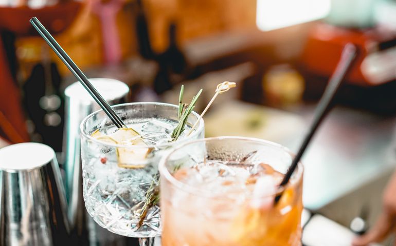 Cocktails served on bar counter prepared with gin, rosemary, paper and orange juice - Drink, nightlife, lifestyle concept - Focus on top crystal glass